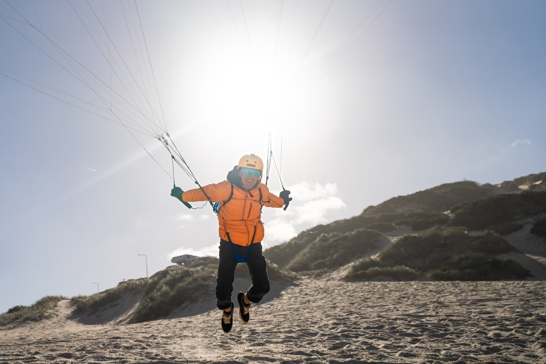 Pilot in an orange jacket handling a wing on the beach